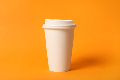 Takeaway paper coffee cup on orange background, closeup