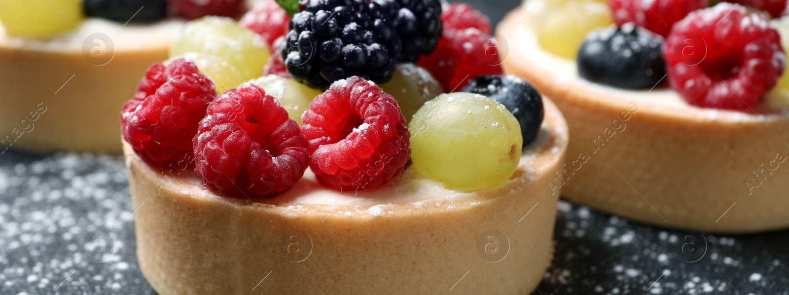 Image of Delicious tartlets with berries on table, closeup. Banner design