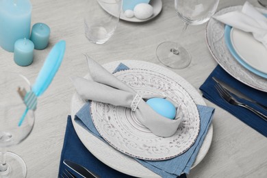 Photo of Festive table setting with bunny ears made of light blue egg and napkin. Easter celebration