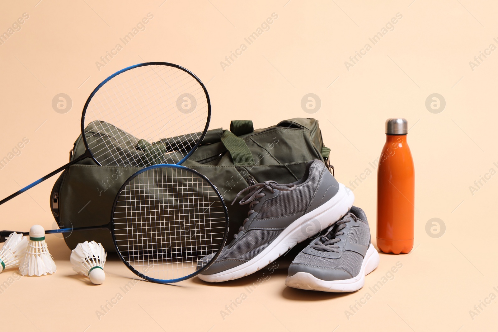 Photo of Badminton set, bag, sneakers and bottle on beige background