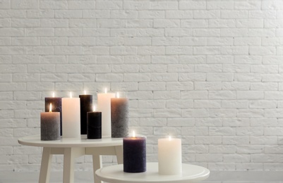 Burning candles on tables against brick wall with space for text