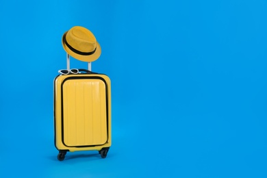 Photo of Travel suitcase with hat and sunglasses on light blue background, space for text. Summer vacation