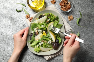 Photo of Woman eating fresh salad with pear at grey table, closeup