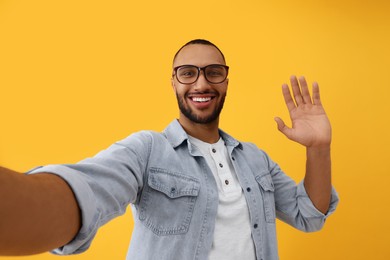 Smiling young man taking selfie on yellow background