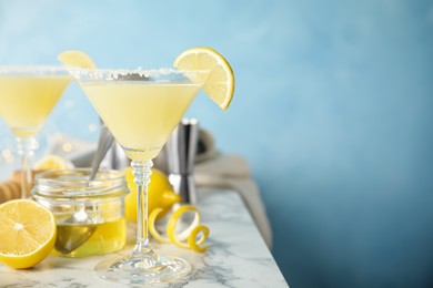 Photo of Delicious bee's knees cocktails and ingredients on white marble table against light blue background. Space for text