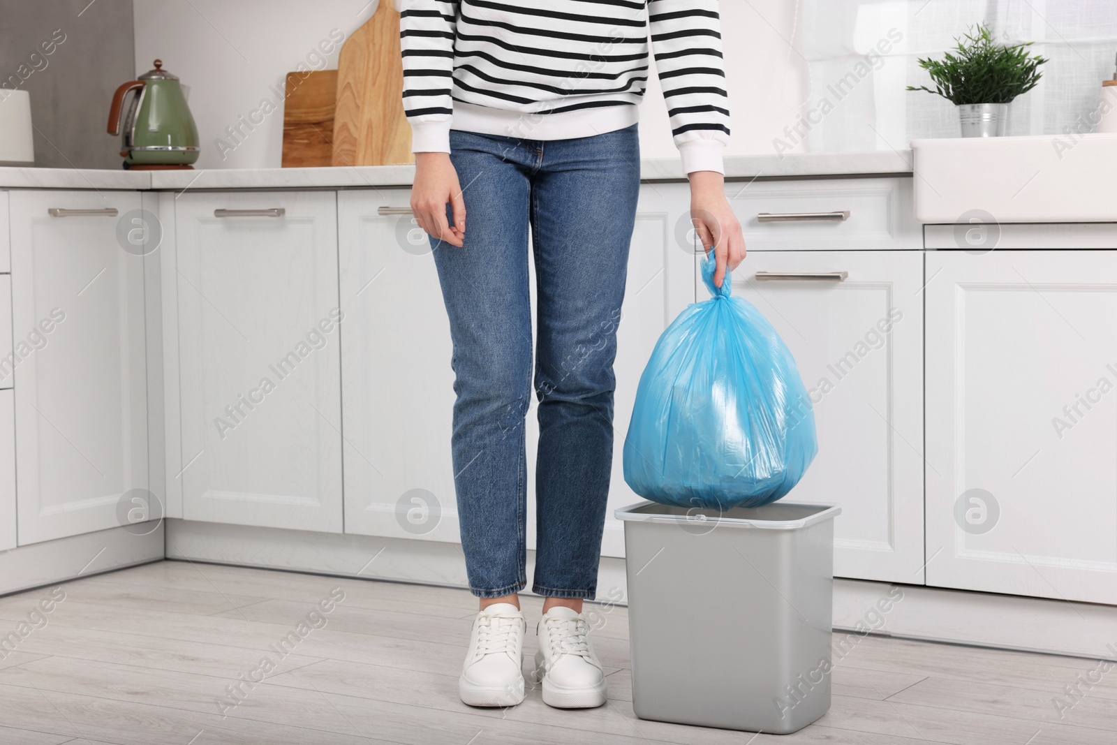 Photo of Woman taking garbage bag out of trash bin in kitchen, closeup