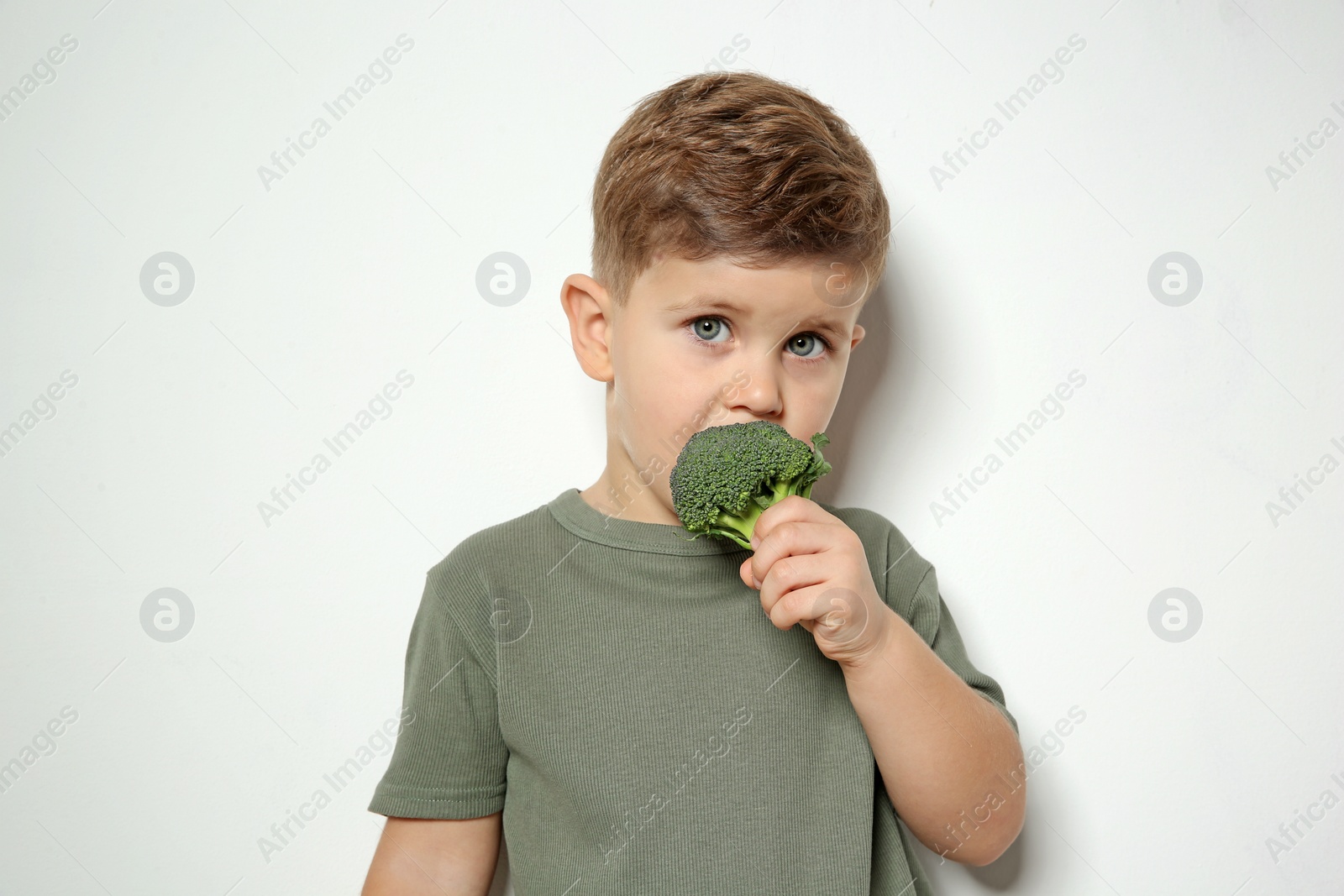 Photo of Adorable little boy eating broccoli on white background