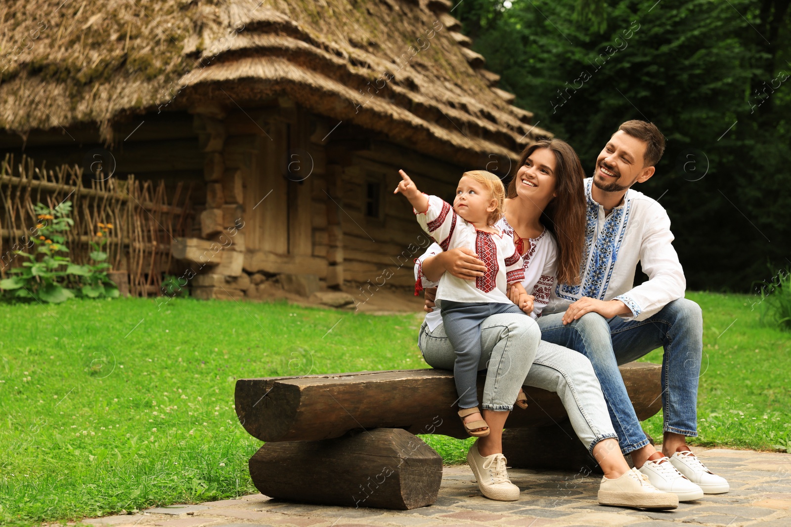 Photo of Happy family in Ukrainian national clothes sitting on bench outdoors