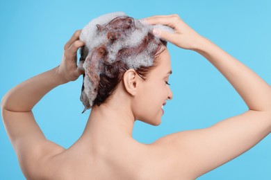 Photo of Young woman washing her hair with shampoo on light blue background, back view