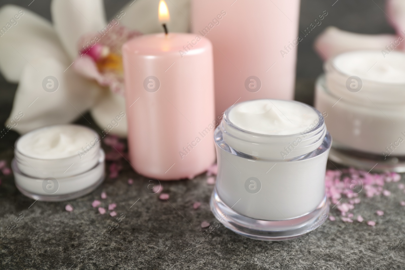 Photo of Beautiful spa composition with cosmetic products, candle and flower on grey table, closeup