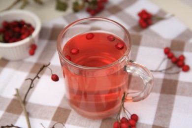 Cup with hawthorn tea and berries on table, closeup