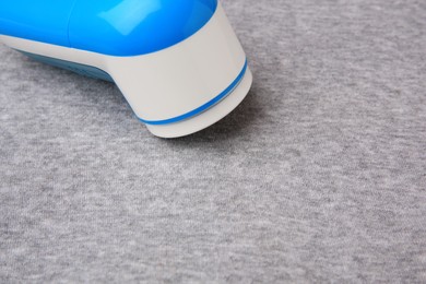 Photo of Modern fabric shaver on light grey cloth with lint, closeup. Space for text