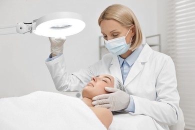 Dermatologist examining patient`s face under lamp in clinic