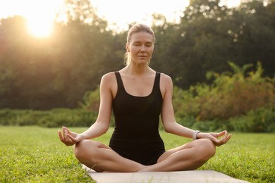 Beautiful woman practicing yoga on mat outdoors. Lotus pose