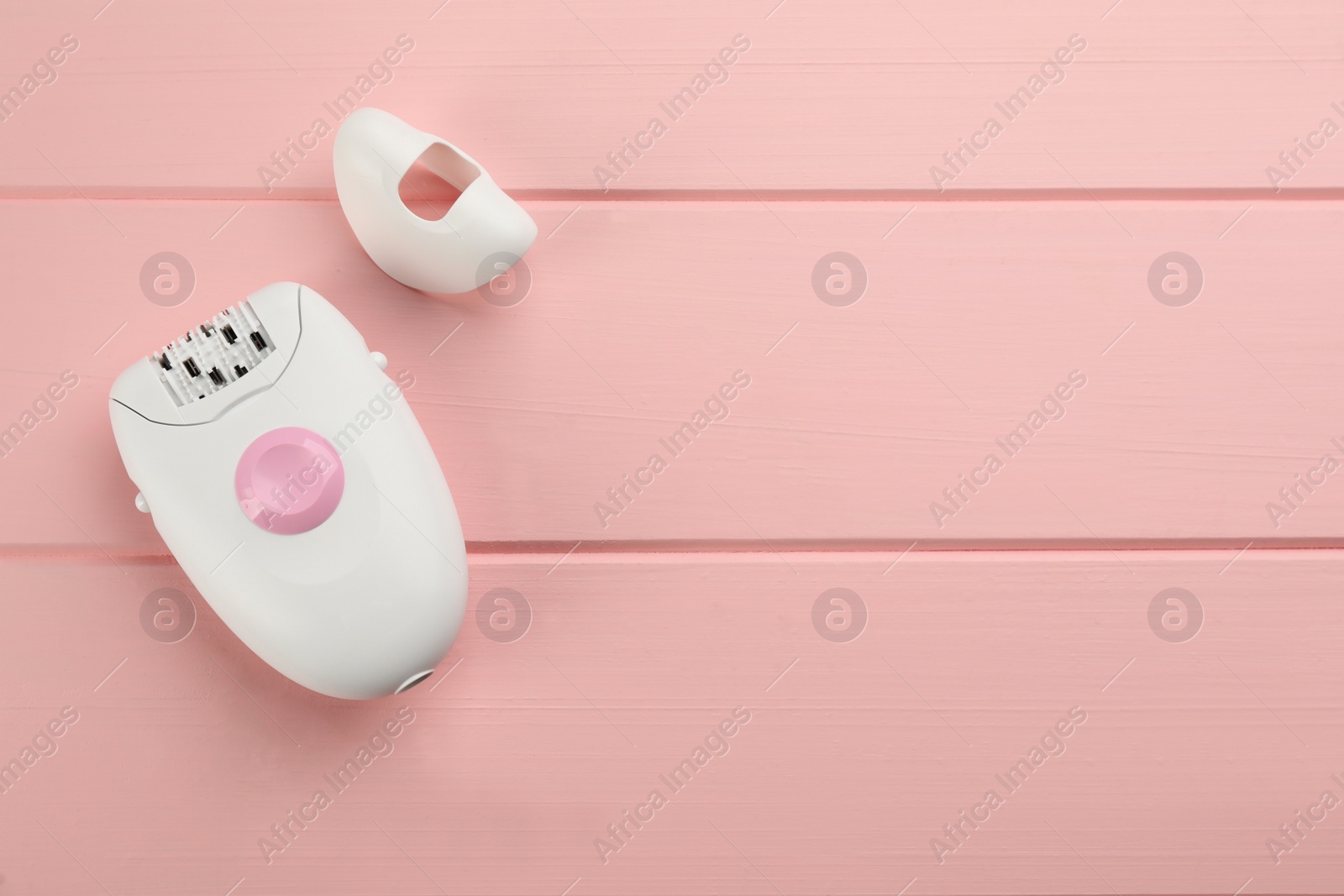 Photo of Modern epilator and cap on pink wooden table, flat lay. Space for text