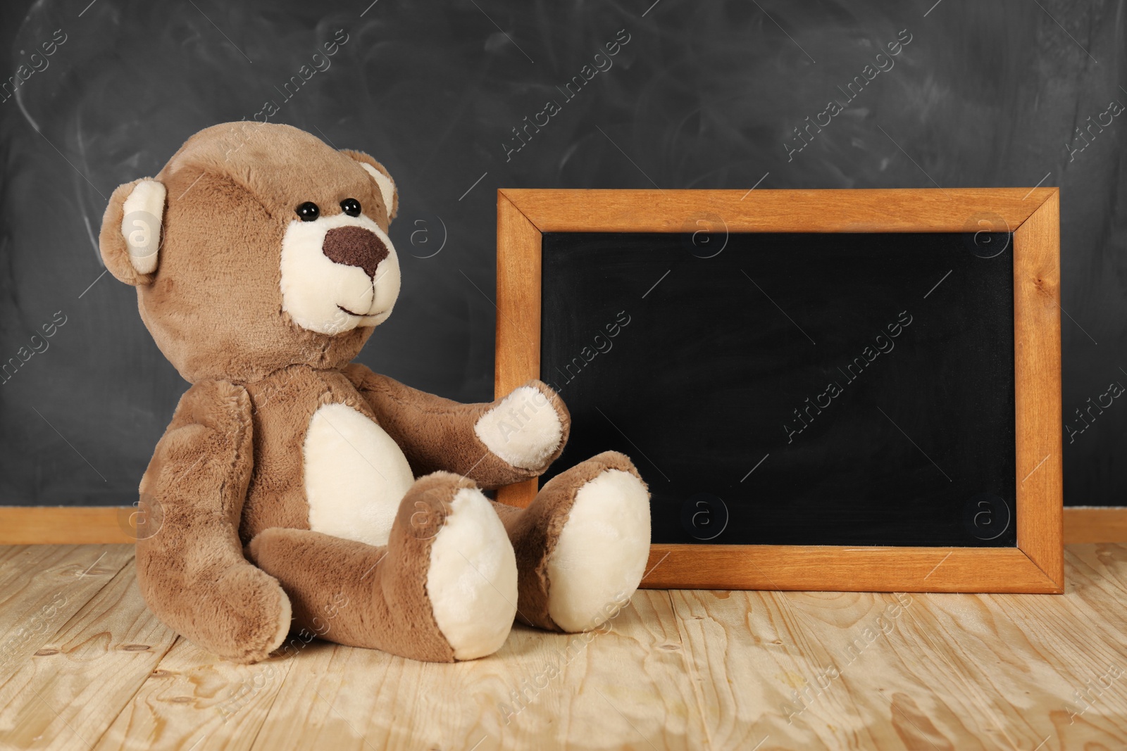 Photo of Teddy bear and small blackboard on wooden table. Space for text