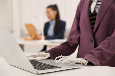 Photo of Human skeleton in suit using laptop at table in office, closeup