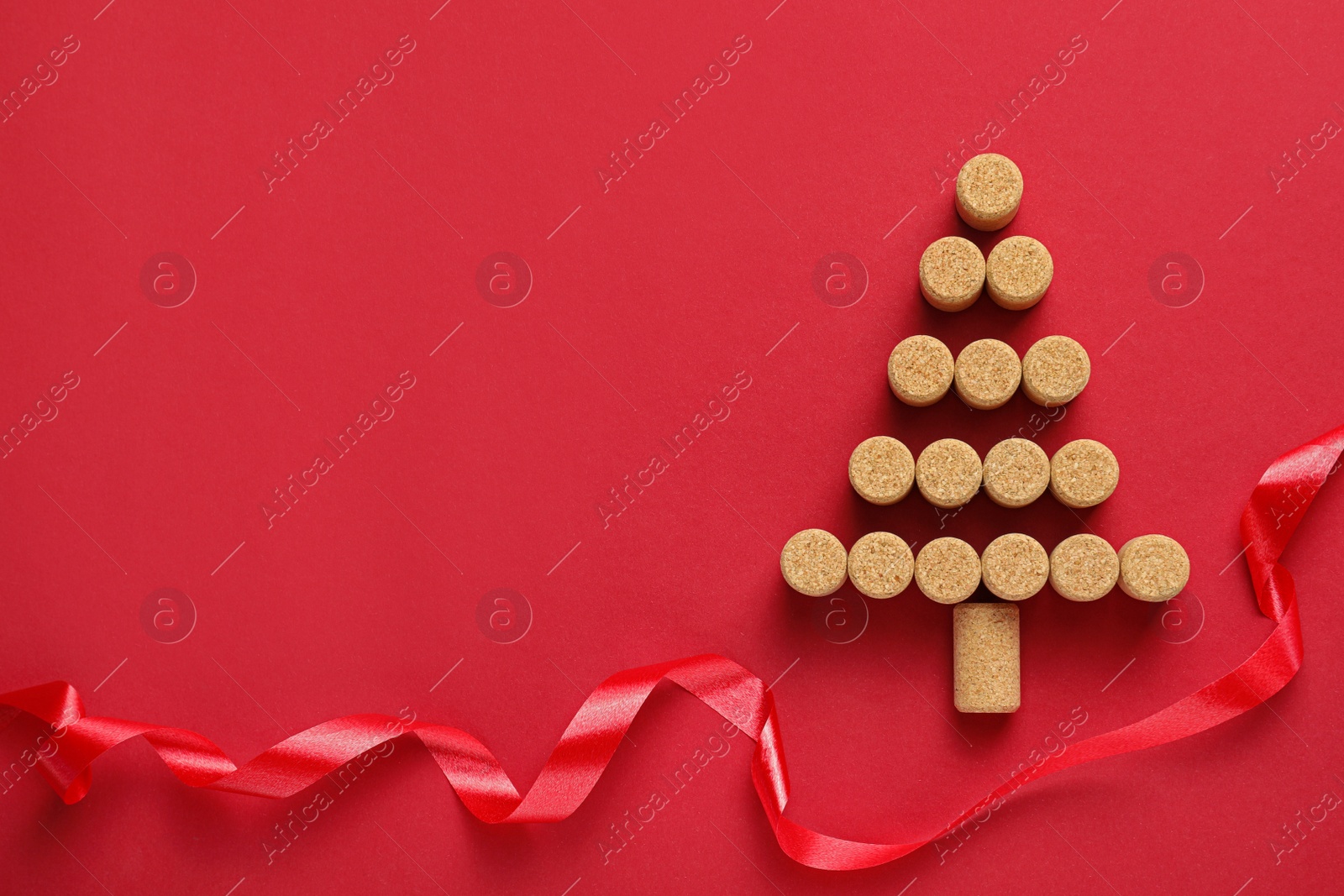 Photo of Christmas tree made of wine corks and ribbon on red background, flat lay. Space for text