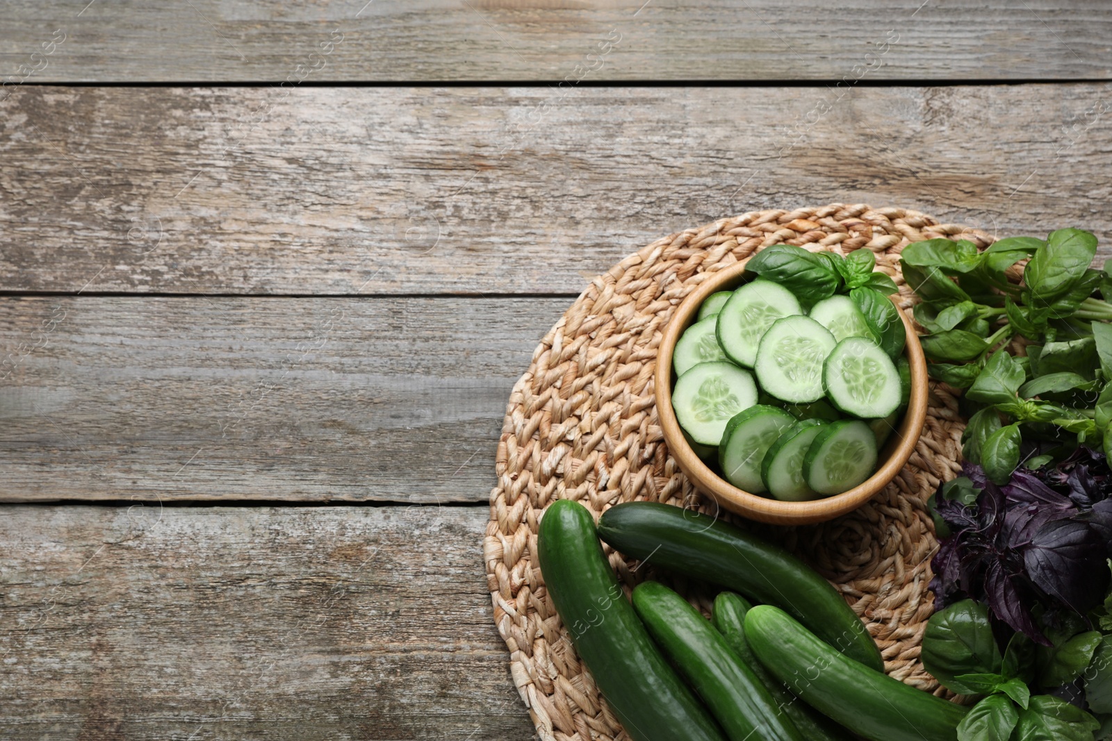 Photo of Fresh ripe cucumbers and greens on wooden table, flat lay. Space for text