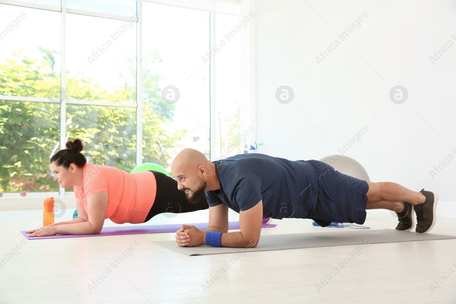 Photo of Overweight man and woman doing plank exercise on mats in gym