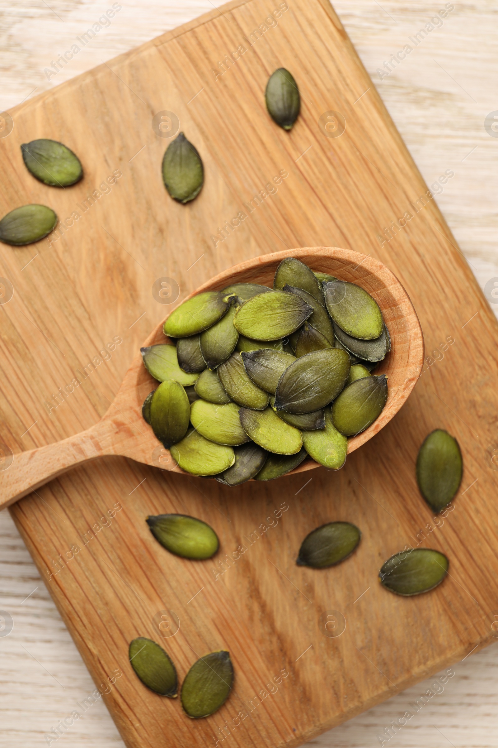 Photo of Spoon with pumpkin seeds on wooden table, top view