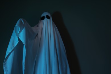 Photo of Creepy ghost. Woman covered with sheet on dark background, space for text
