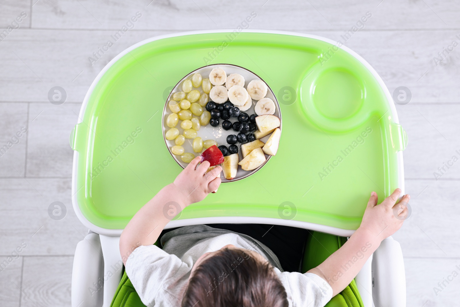 Photo of Cute little baby eating healthy food in high chair indoors, top view