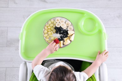 Cute little baby eating healthy food in high chair indoors, top view