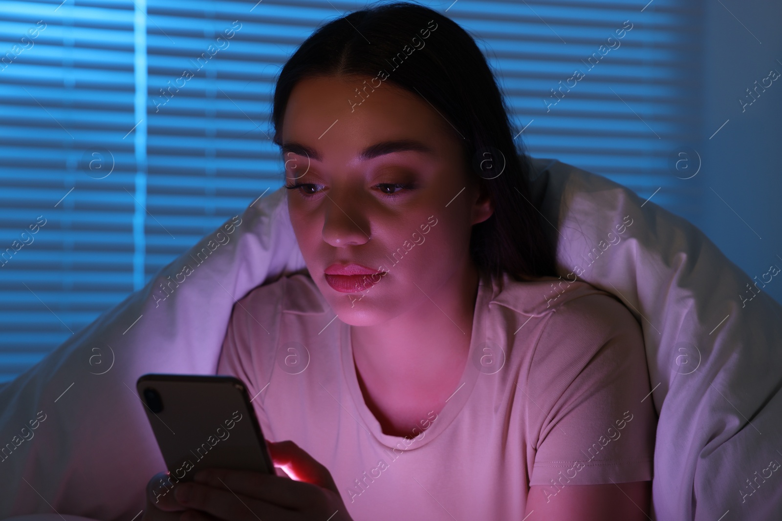 Photo of Young woman using modern smartphone in bed at night. Internet addiction