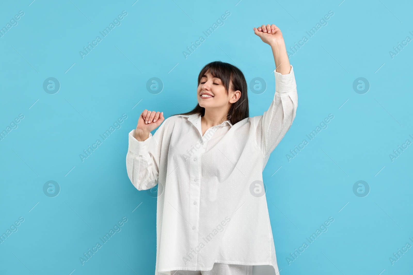 Photo of Woman in pyjama stretching on light blue background