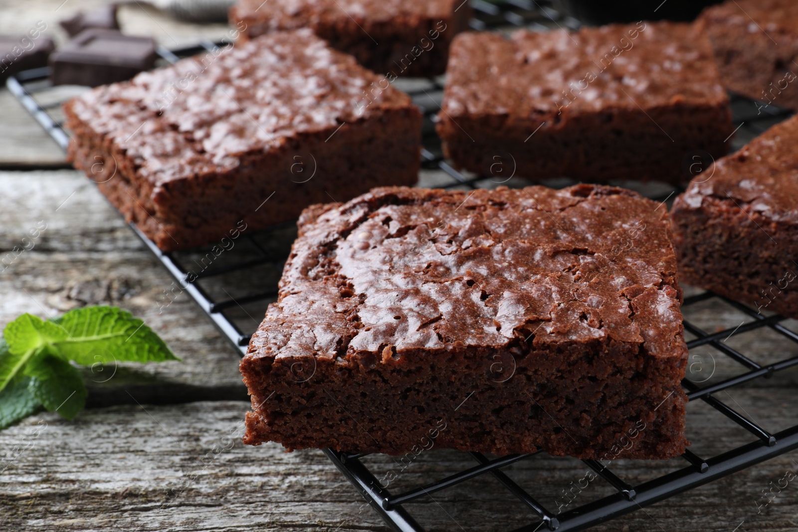 Photo of Cooling rack with delicious chocolate brownies and fresh mint on wooden table, closeup