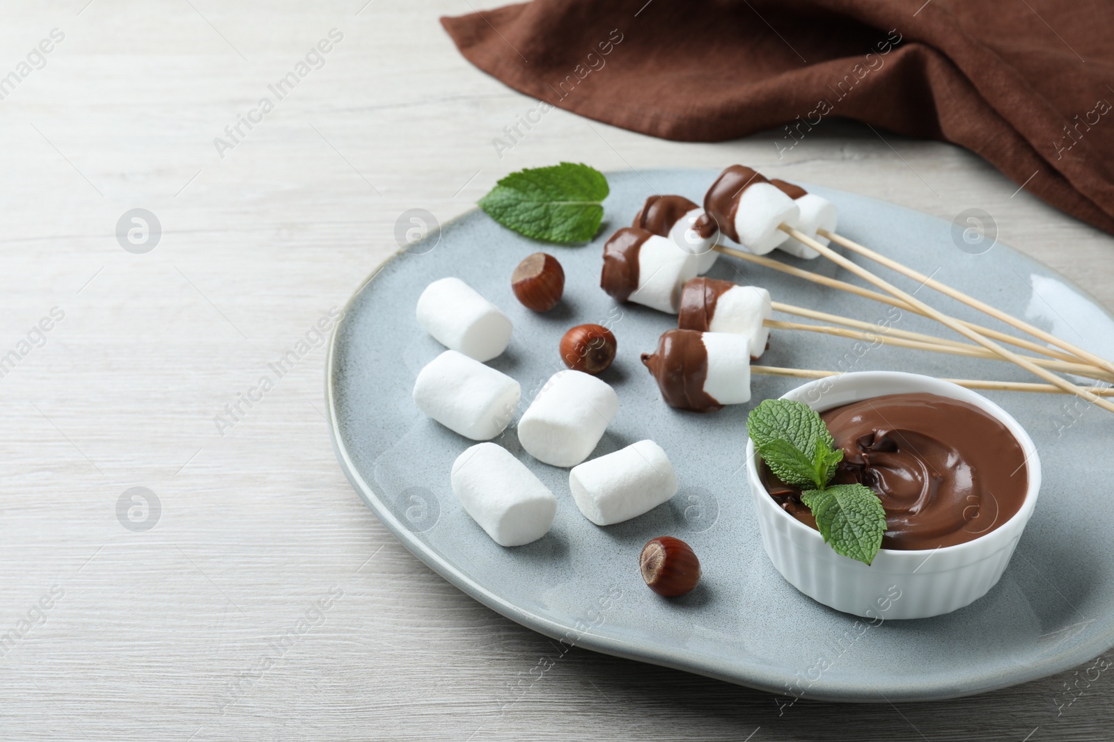 Photo of Bowl with melted chocolate and marshmallows on white wooden table