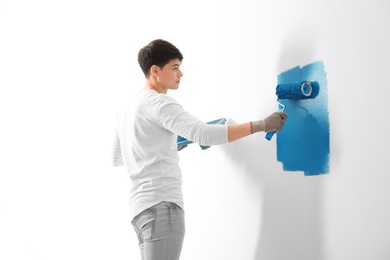 Male decorator painting wall with roller indoors