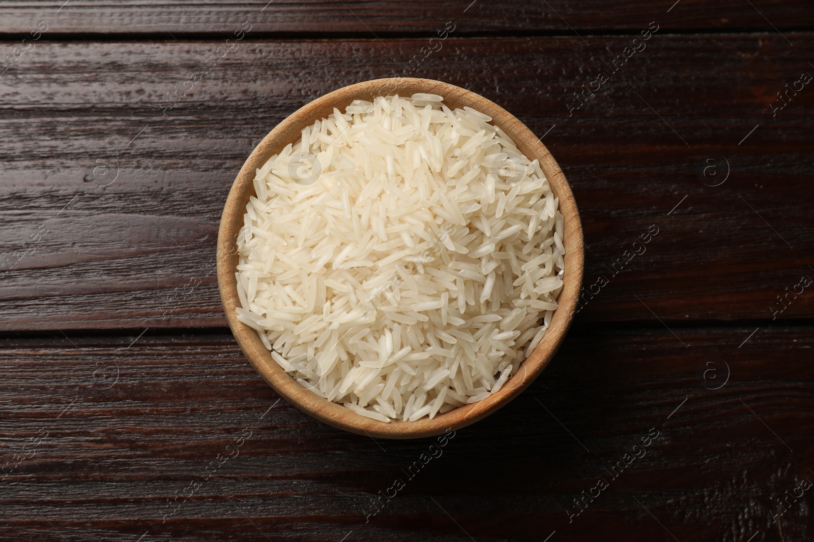 Photo of Raw basmati rice in bowl on wooden table, top view