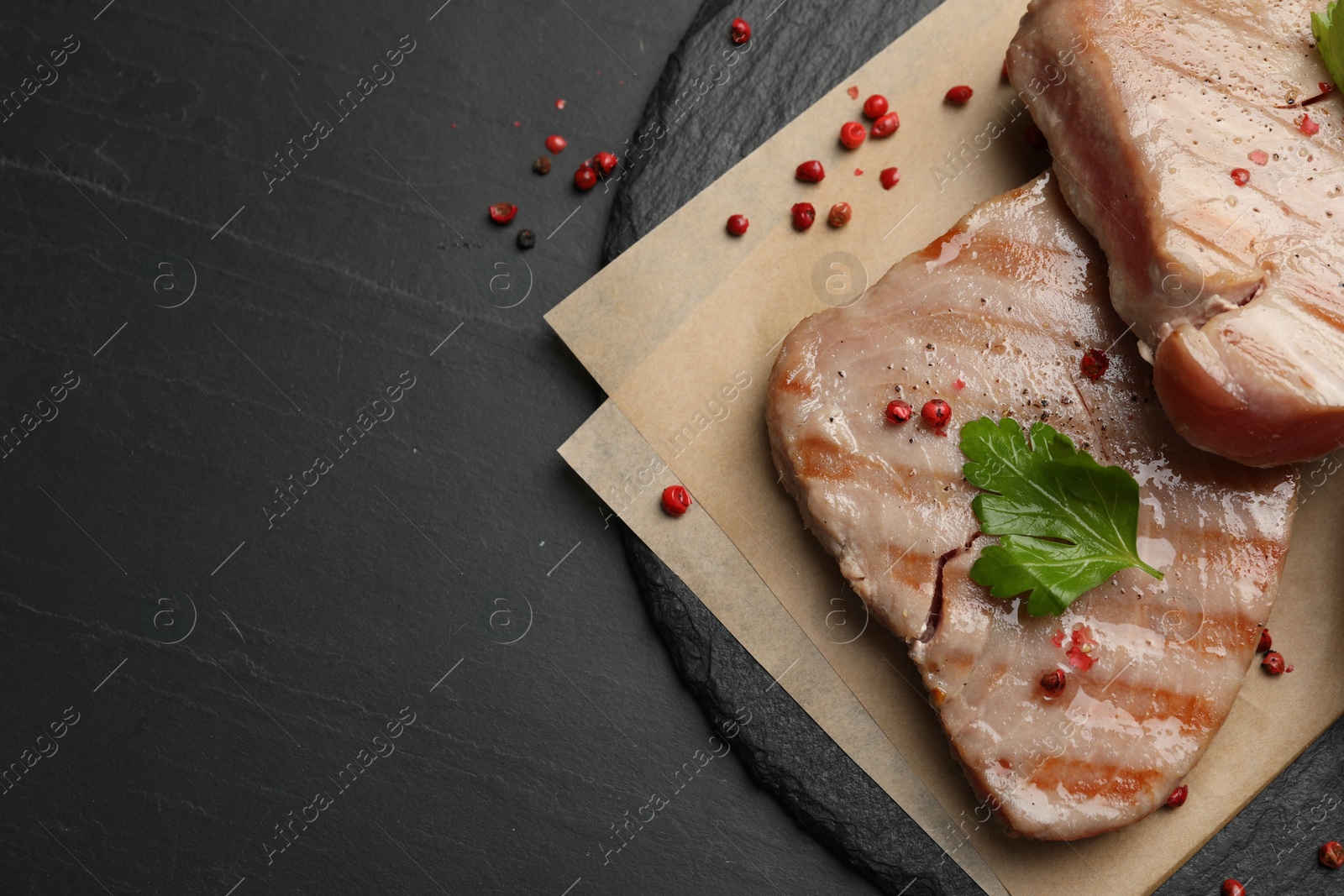 Photo of Delicious tuna steaks with parsley and spices on black table, top view. Space for text