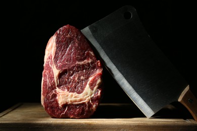 Piece of raw beef meat and knife on wooden board against black background
