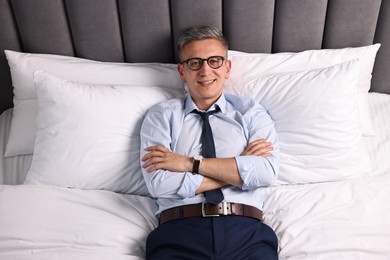 Businessman in glasses lying on bed indoors, above view