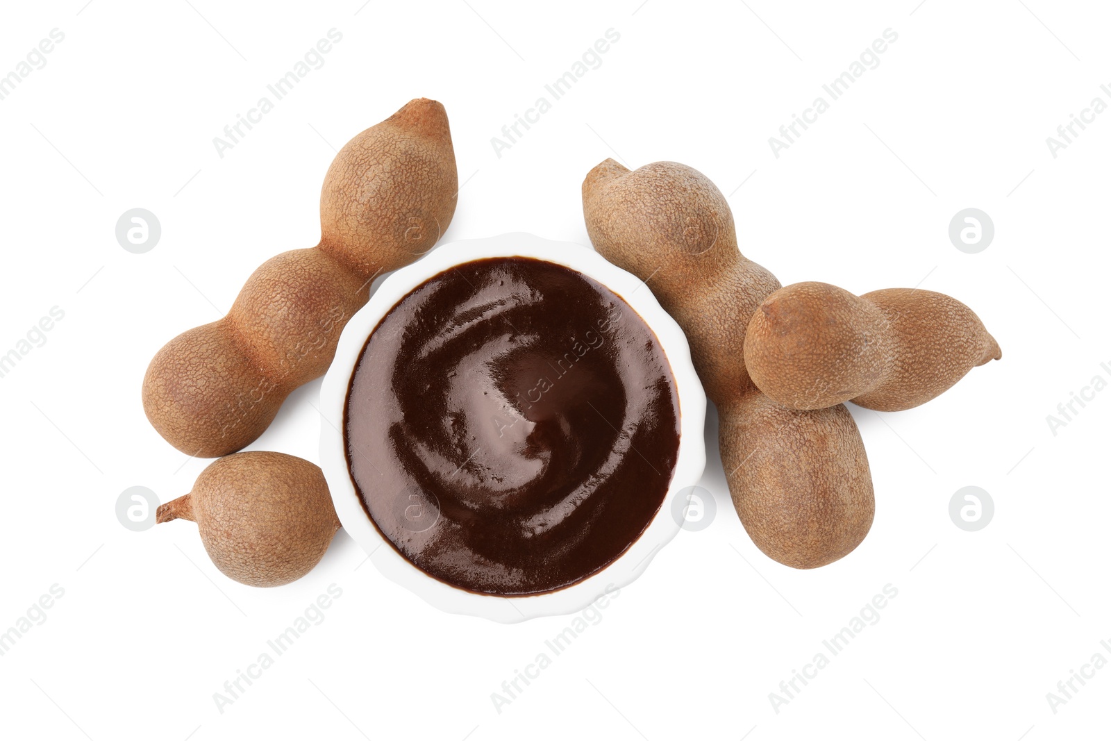 Bowl of tasty tamarind sauce and fresh pods isolated on white, top view Photo of Bowl of tasty tamarind sauce and fresh pods isolated on white, top view