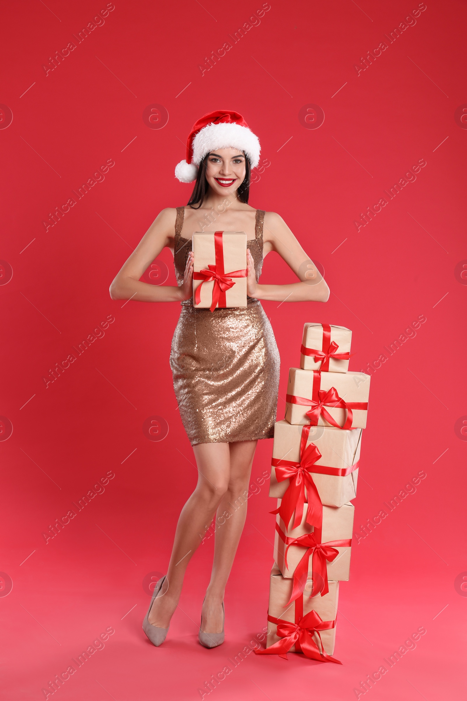 Photo of Woman in golden dress and Santa hat with Christmas gifts on red background