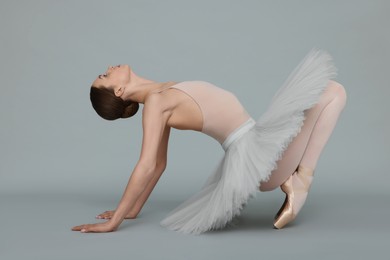 Photo of Young ballerina practicing dance moves on light grey background