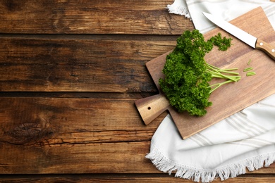 Photo of Fresh curly parsley, cutting board and knife on wooden table, flat lay. Space for text