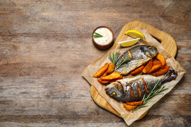 Photo of Delicious roasted fish and potatoes on wooden table, flat lay. Space for text