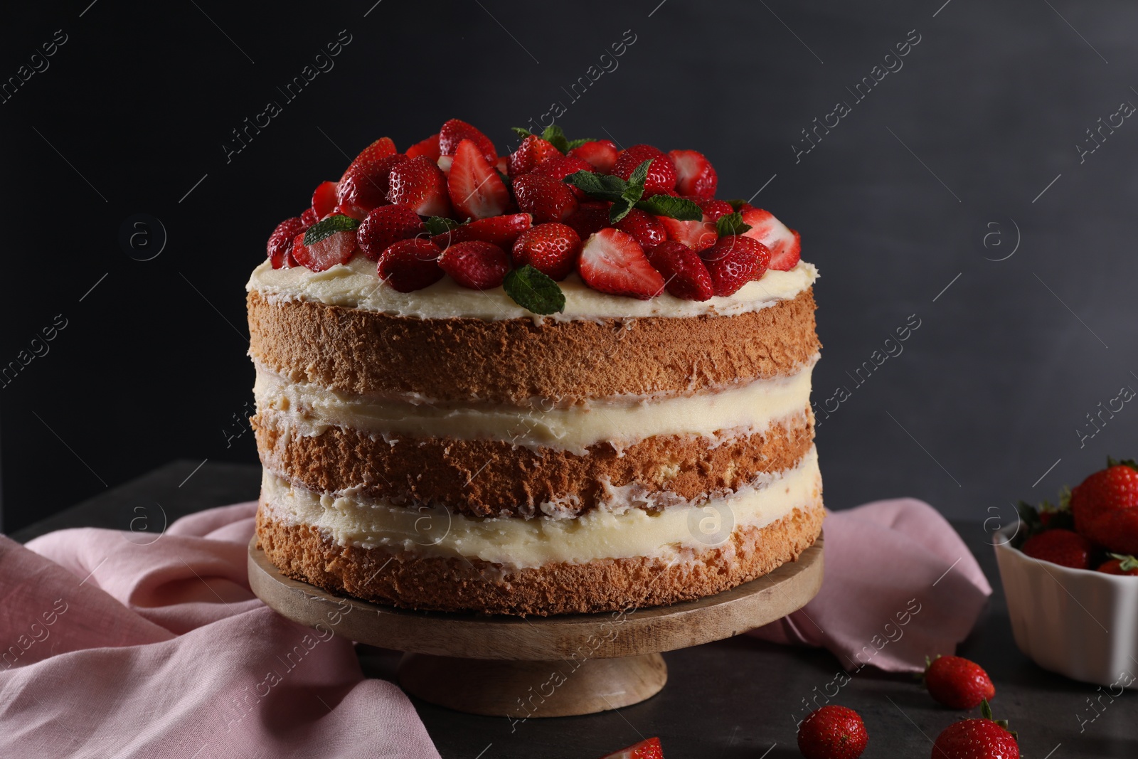 Photo of Tasty cake with fresh strawberries and mint on table against dark gray background