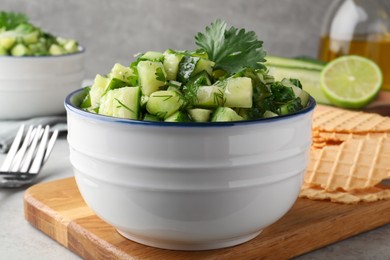 Photo of Bowl of delicious cucumber salad served on light table, closeup