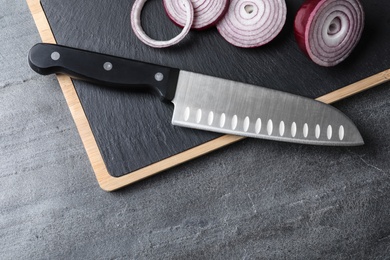 Board with sharp knife and cut onion on grey background, flat lay