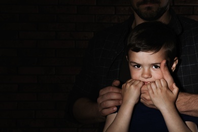 Photo of Adult man covering despaired little boy's mouth on dark background, space for text. Child in danger