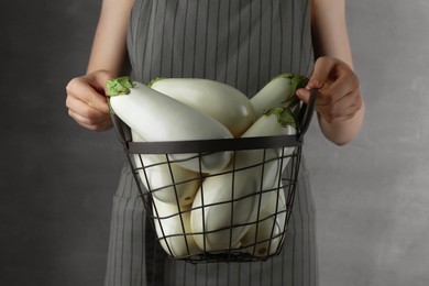 Photo of Woman holding metal basket with white eggplants on grey background, closeup