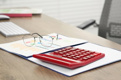 Photo of Calculator, documents and glasses on wooden desk in office, closeup
