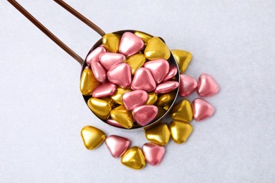 Metal scoop and delicious heart shaped candies on white table, flat lay