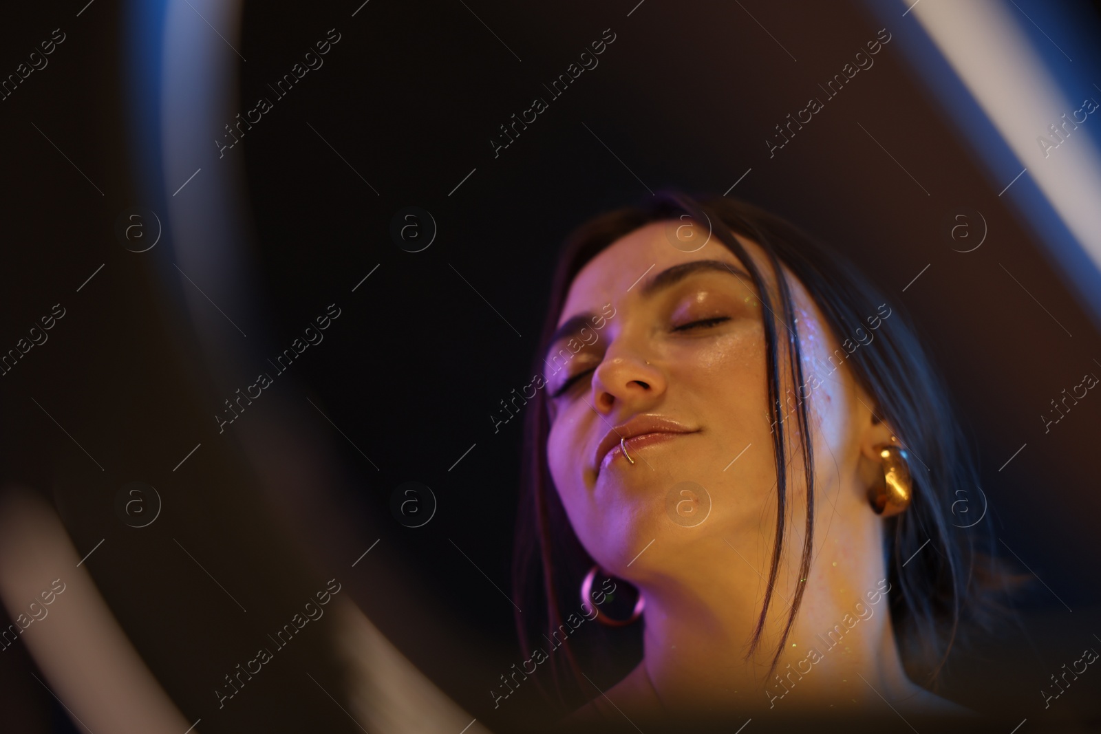 Photo of Portrait of beautiful woman on dark background in neon lights, view through ring lamp